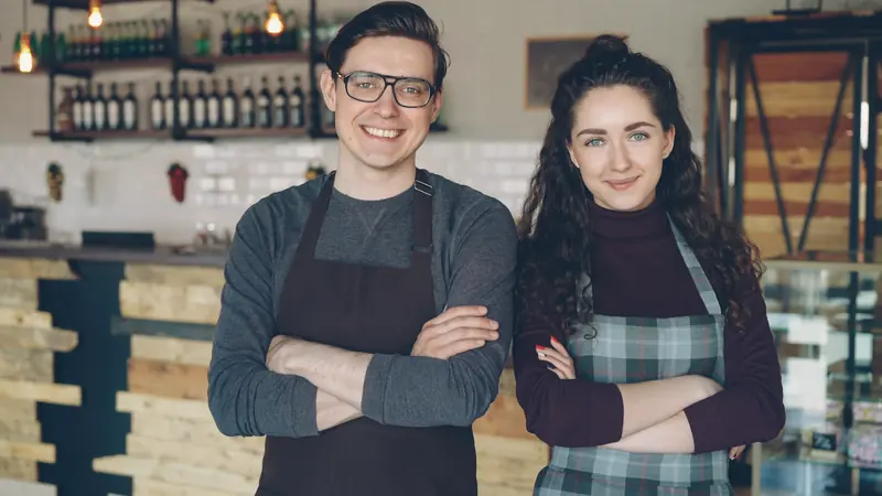 Dos dueños de una cafetería posan sonrientes detrás del mostrador.
