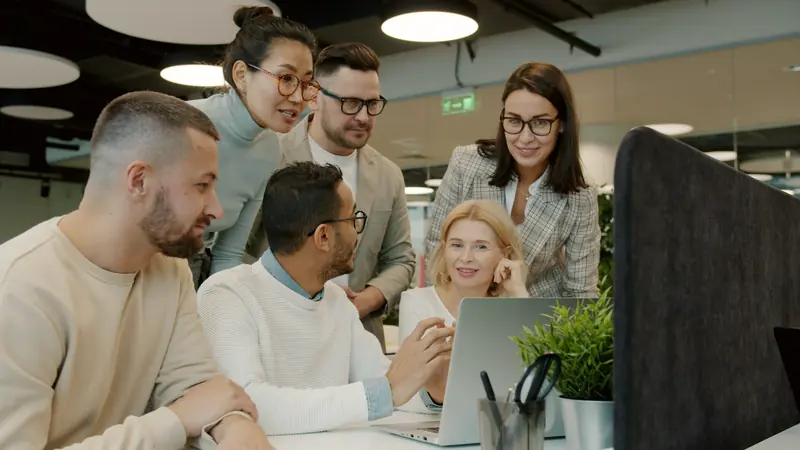 Un equipo de trabajo revisa algo juntos alrededor de un portátil.